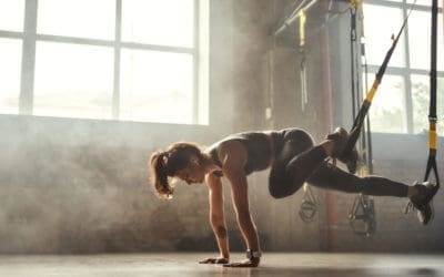TRX Training. Young athletic woman in sports clothing training legs with trx fitness straps in the gym.